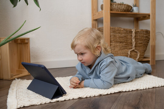 Cute toddler lying on floor and watching video on tablet