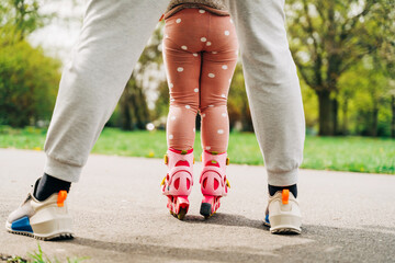Crop faceless child roller skating in park with help of anonymous parent