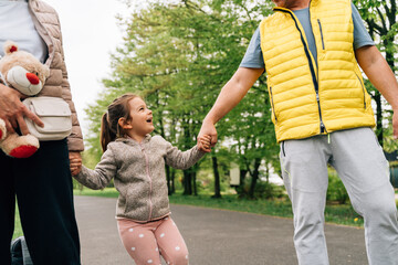 Cheerful little kid holding hands of grandparents in park