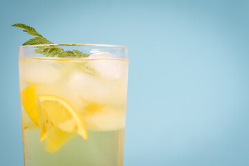 Close up of ice tea in a highball glass with lemon, ice, and mint on a blue background