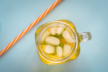 Aerial photo of ice tea in a glass jar with ice, lemon, and mint on a blue surface with red and...