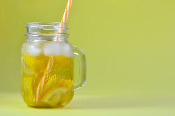 Glass jar of ice tea filled with ice and lemon and red and white straw