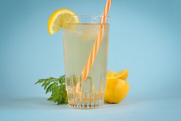 Ice tea in a highball glass decorated with mint and lemon and a red and white straw on a blue...