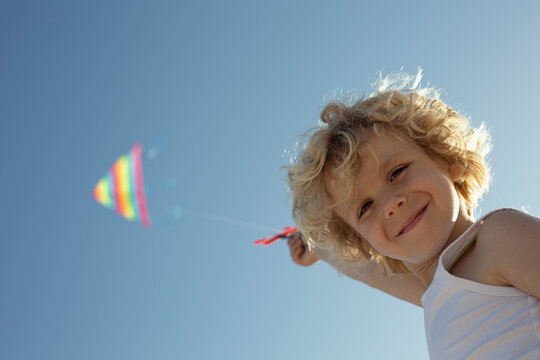 Cheerful child smiling and camera while launching colorful kite