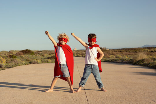 Cute positive kids in superhero costumes standing on road with raised fists