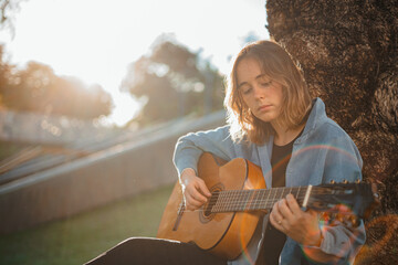 Back-lit shot of young woman concentrated while playing the guitar at the park.