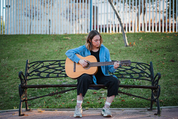Teenage girl seems focus playing the guitar while sitting on a bench at the park