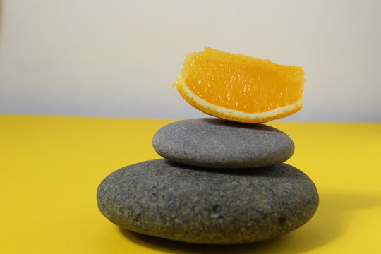 a ballans tower of grey stones and grapefruit orange fruit on a white yellow background with room for text. Benefits of Energy Health Importance Vitamin