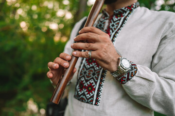 Hands of young man playing on woodwind wooden flute - ukrainian sopilka outdoors. Folk music concept. Musical instrument. Musician in traditional embroidered shirt - Vyshyvanka. © kohanova1991