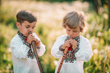 Little brothers boys playing on woodwind wooden flute - ukrainian sopilka outdoors. Folk music...