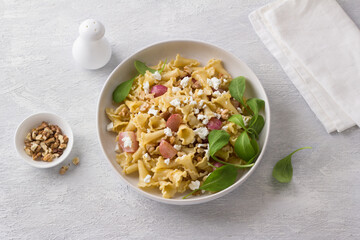 Italian pasta campanelle with radishes, feta cheese, walnuts and arugula in a white plate on a light gray background
