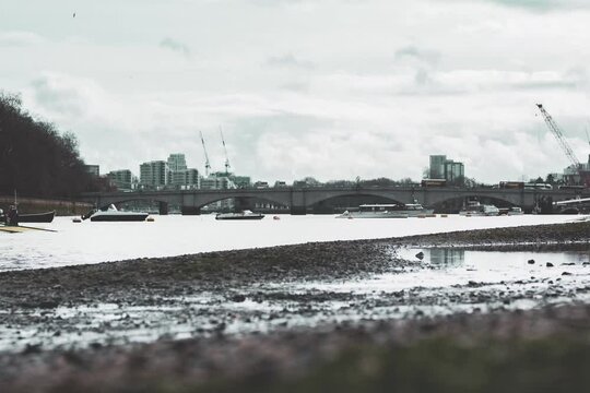 timelapse of Putney Bridge and River Thames river and shingle shore bank with boats on water and blue sky 4K UHD