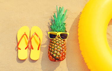 Summer vacation concept - pineapple and inflatable ring with yellow flip flops on the beach on sand...