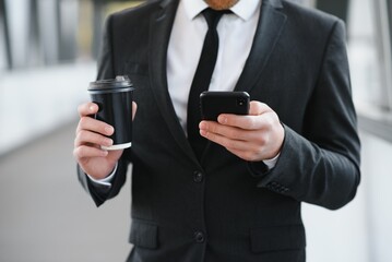 Confident young businessman using cell phone and drinking coffee in the city