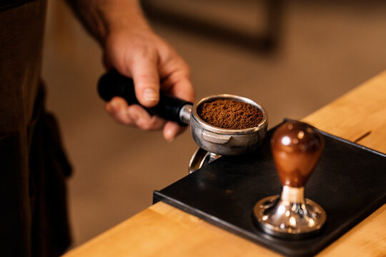 Crop anonymous man using tamper for pressing ground coffee in portafilter