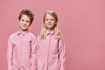 two beautiful children a boy and a girl are standing in pink clothes on a pink background