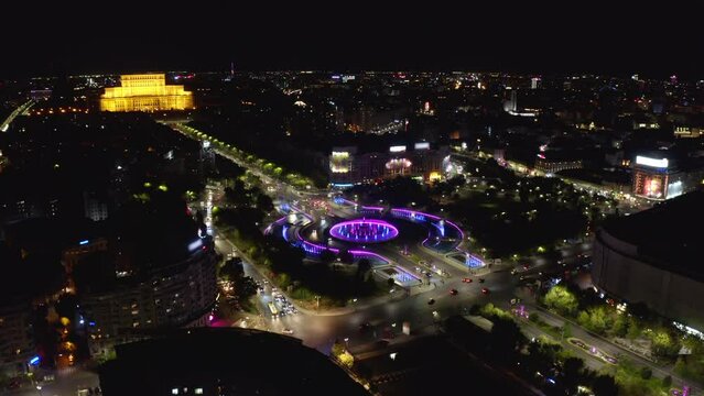 4k night aerial footage of a view of the parliament of the Romanian capital Bucharest and Unirii Boulevard with luminous round fountains and cars passing through the city at night. Glowing nightlife.