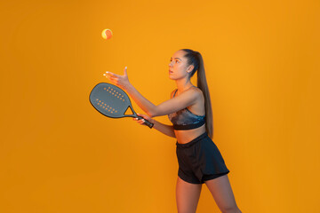 Young girl playing beach tennis on yellow color background . Professional sport concept. Horizontal...