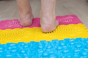 A woman with varicose veins and cracked heels walks on a colorful massage mat. Close-up. soft focus