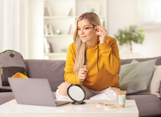 Casual young woman applying mascara and watching make up tutorials on a laptop computer