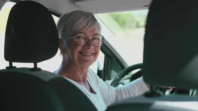 Happy owner. Handsome mature woman sitting relaxed in his newly bought car looking at the camera smiling joyfully. One old senior driving and having fun.
