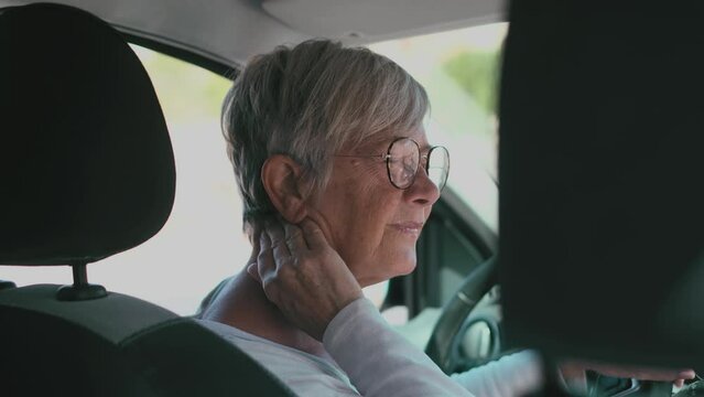 Rear view of old woman having neck pain while driving a car. One senior or mature people feeling bad for injury.
