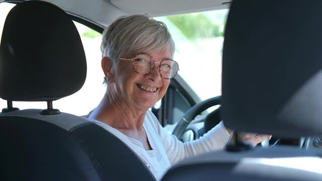 Happy owner. Handsome mature woman sitting relaxed in his newly bought car looking at the camera smiling joyfully. One old senior driving and having fun.
