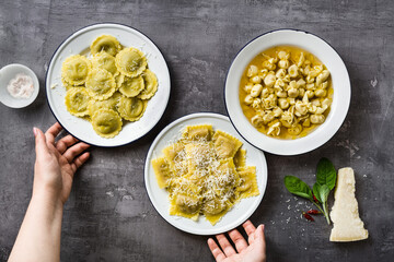 several types of boiled italian ravioli in plates on the table. homemade serving with parmesan cheese and female hands