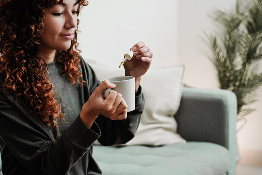 Cbd hemp oil - Woman taking cannabis oil in tea cup - Focus on hand holding droppler