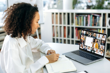 Online learning concept. Positive smart dark-skinned girl, sits in the library, in front of the...