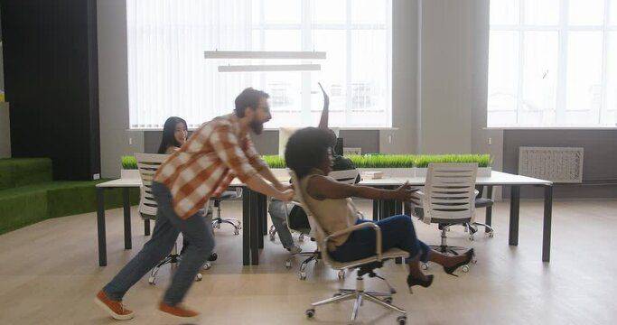 Man pushes African American woman in rolling chair in office