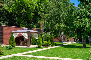 Backyard with a green lawn and a gazebo near the green trees
