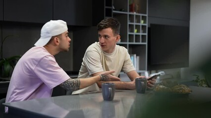 Irritated gay man arguing with boyfriend distracting partner from surfing social media on smartphone. Portrait of annoyed Caucasian LGBTQ couple quarreling in kitchen at home indoors