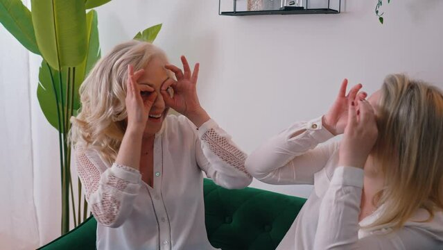 Two middle-aged caucasian women having fun together, making owl sign with fingers and hands. Indoor apartment shot. High quality 4k footage