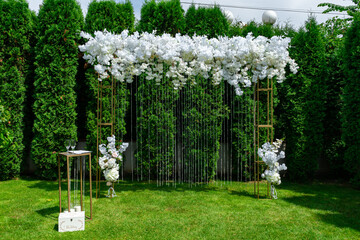 White wedding arch on a background of evergreen thuja. Summer wedding ceremony in the park