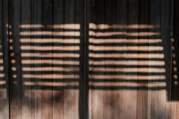 Shadows and sunlight on a brown wooden wall. Beams of sunlight through old window wooden blinds.