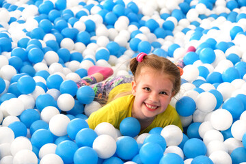 Little happy girl playing in dry pool with plastic balls. Close-up leisure activities indoors....