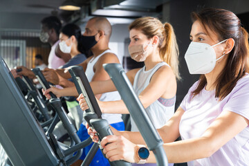 Slim athletic people in protective masks running on treadmill in a fitness club