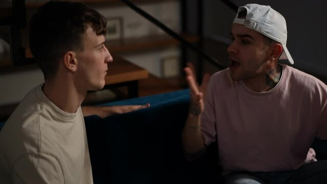 Portrait of annoyed irritated gay man shouting gesturing arguing with partner indoors. Displeased Caucasian LGBTQ person quarreling with boyfriend in living room at home at night
