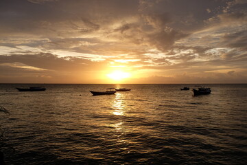 Sunset view with silhouette of fishing boats in the ocean. Warm colored sky with beautiful clouds.