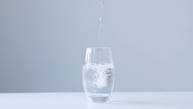 Pouring pure water into glass on light gray background, super slow motion. Clear fresh drinking water filling glass. Quenching thirst concept
