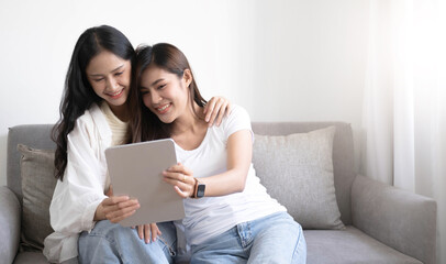 Young beautiful Asian women lesbian couple lover using tablet video call online in living room on sofa at home with smiling face.Concept of LGBT sexuality with happy lifestyle together.
