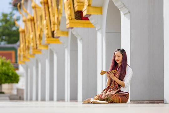 Asian buddhist woman is reading Sanskrit ancient palm leaf manuscript of Tripitaka the Lord Buddha dhamma teaching while sitting in temple on holy full moon day to chant and worship in the monastery