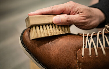 Hand holding walnut wood brush cleaning dirt and dust on brown leather shoe. A man take care of luxury vintage footwear by soft crafted hog’s hair bristle, maintenance and protection service concept.