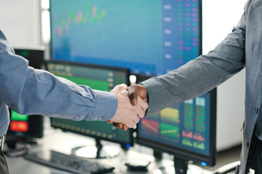 Unrecognizable African American stock trading specialist and his Caucasian client making deal and doing handhsake