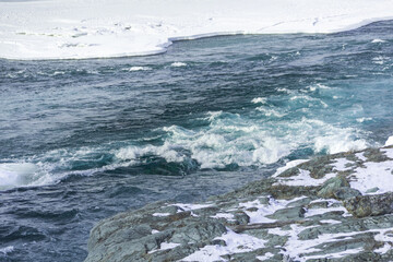 Blue winter river flows between ice floes. Arctic landscape on sunny day. Water boils and forms ripples on sea.