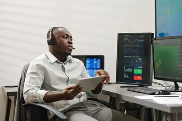 African American man holding digital tablet working with clients advising them best stocks to buy...
