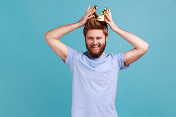 Portrait of happy bearded man wearing golden crown, imagining promotion at work to position,...