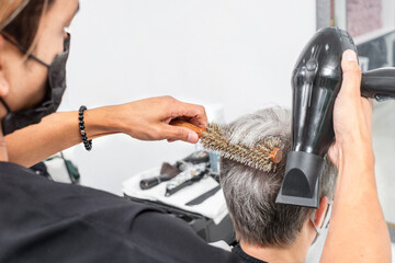 Fototapeta na wymiar Hairdresser dries senior hair