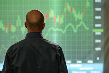 Unrecognizable Mature man working in stock trading company looking at graph, rear view shot